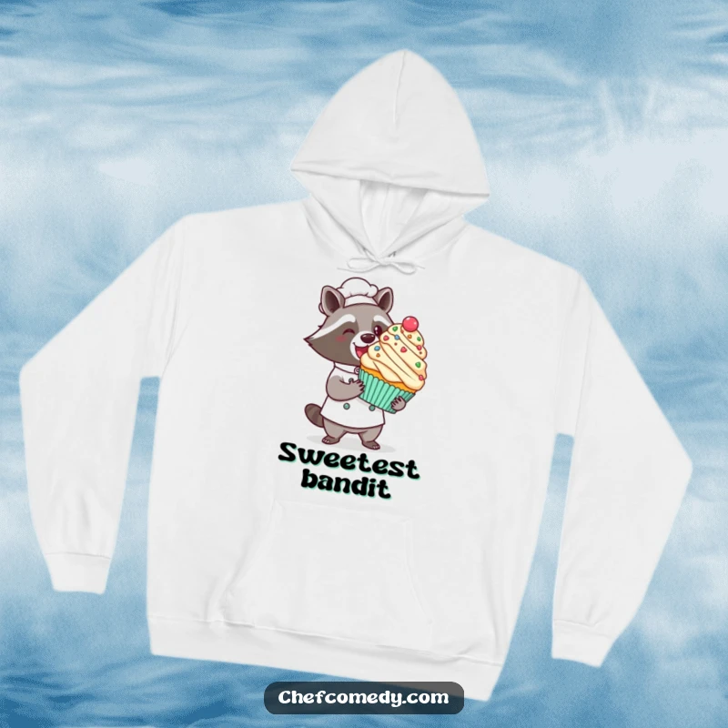 Funny kawaii raccoon chef hoodie, a proud raccoon presenting a giant decorated cupcake with a flourish, cozy bakery attire.