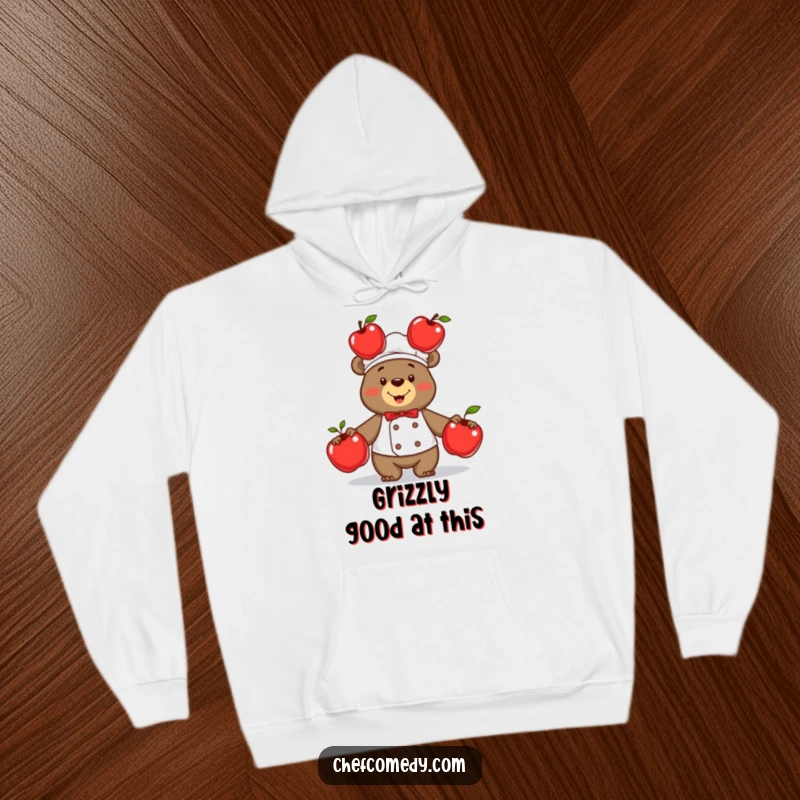 Cozy funny bear chef in action, proudly juggling three shiny red apples with a joyful expression on this warm hoodie.