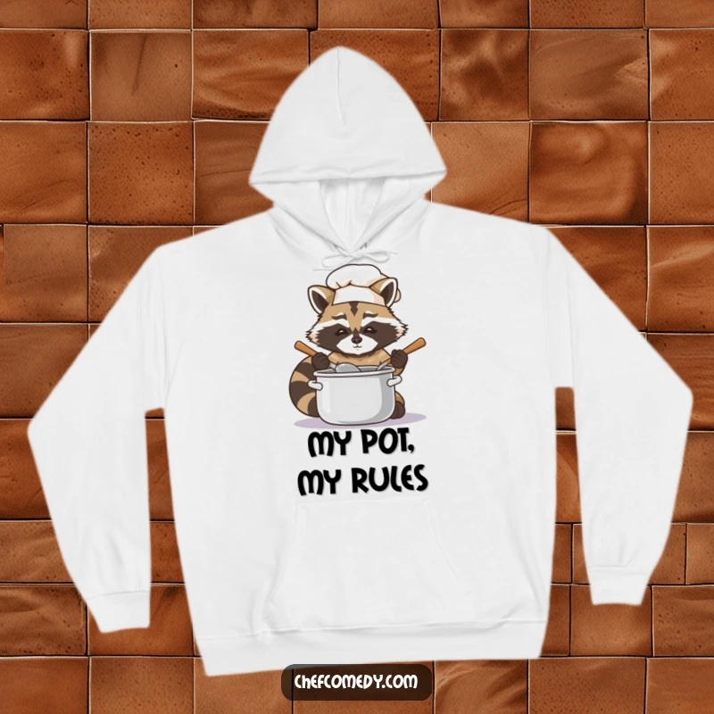 Soft hoodie depicting a funny raccoon chef focused on stirring a pot, blending comfort and culinary humor.